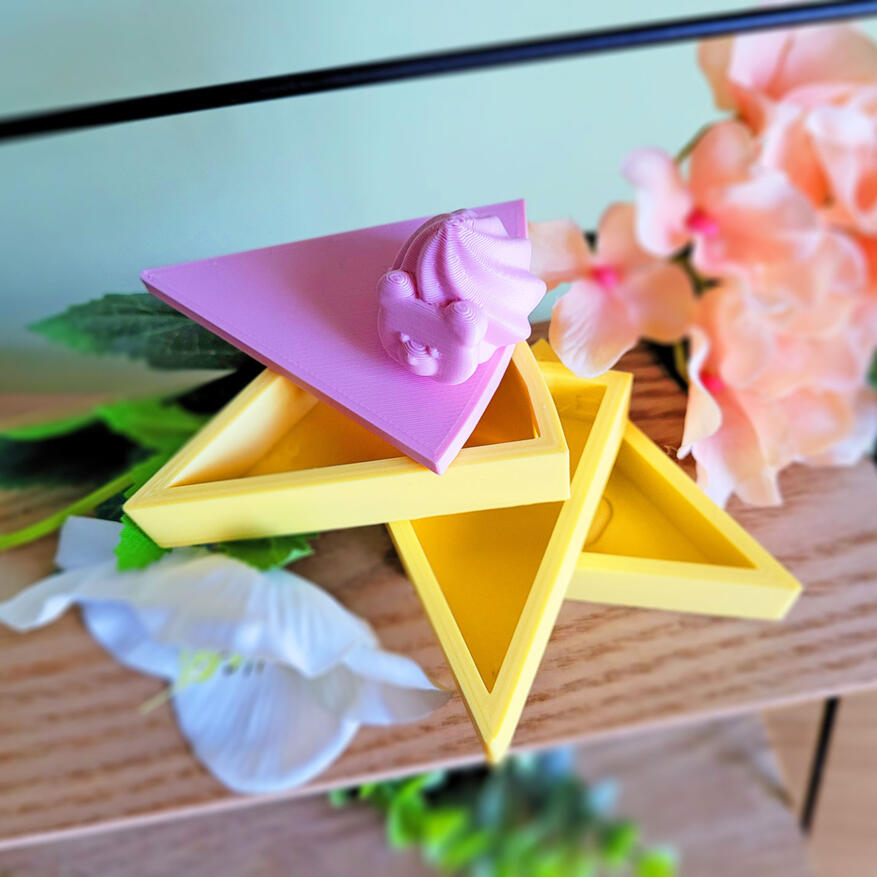 Untitled A pink and yellow 3D printed boxe, modeled to look like a slice of cake. The box has 3 compartments, each one a "layer" of cake. There is a small decoration on the top of it. The box is open, showing how all three compartments swivel around an axis.